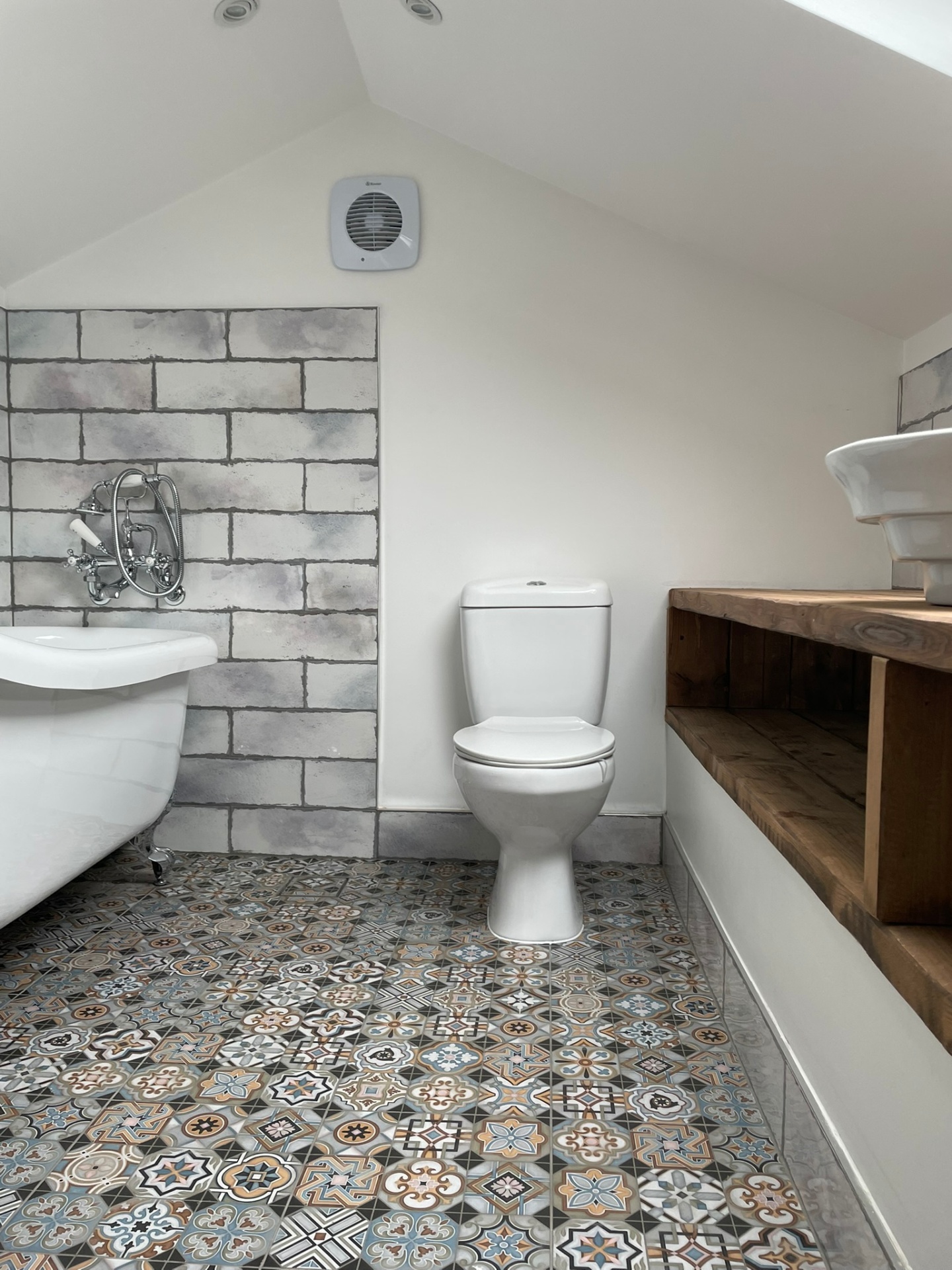 Loft bathroom with sloped ceiling, white roll-top bath on claw feet and patterned floor tiles — Ash Villa bathroom installation, West London