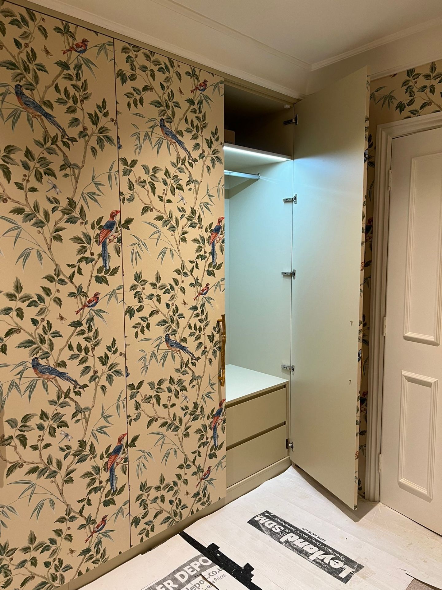 Open section of a patterned fitted wardrobe showing interior drawers and a lit hanging rail — Ash Villa bespoke joinery