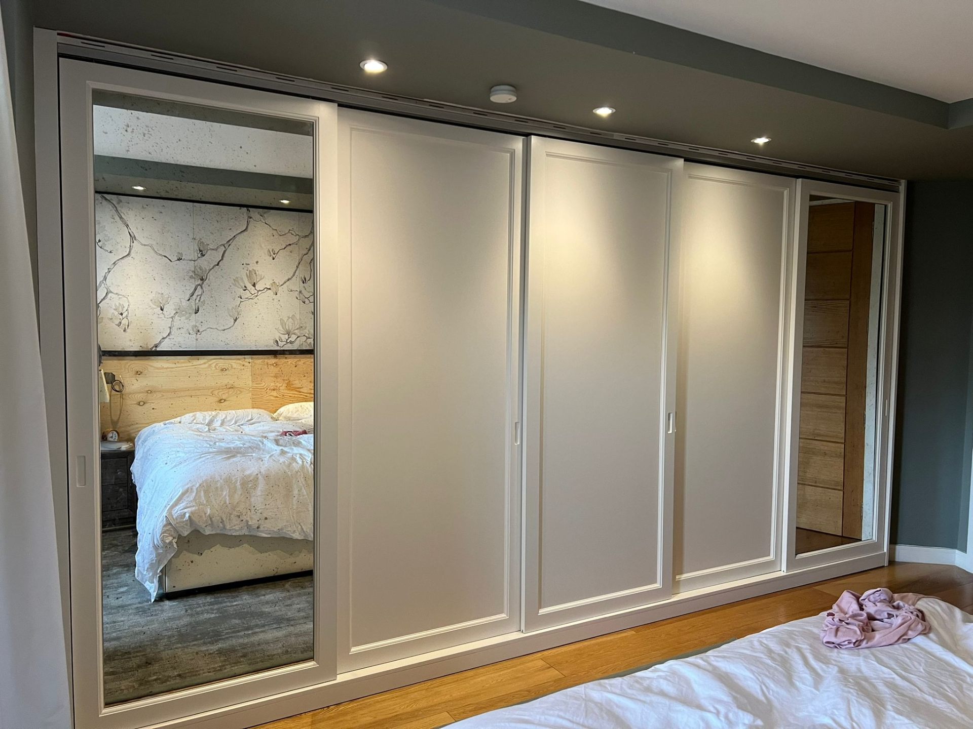 Fitted sliding wardrobe with mirrored end panels and painted shaker doors in a West London master bedroom