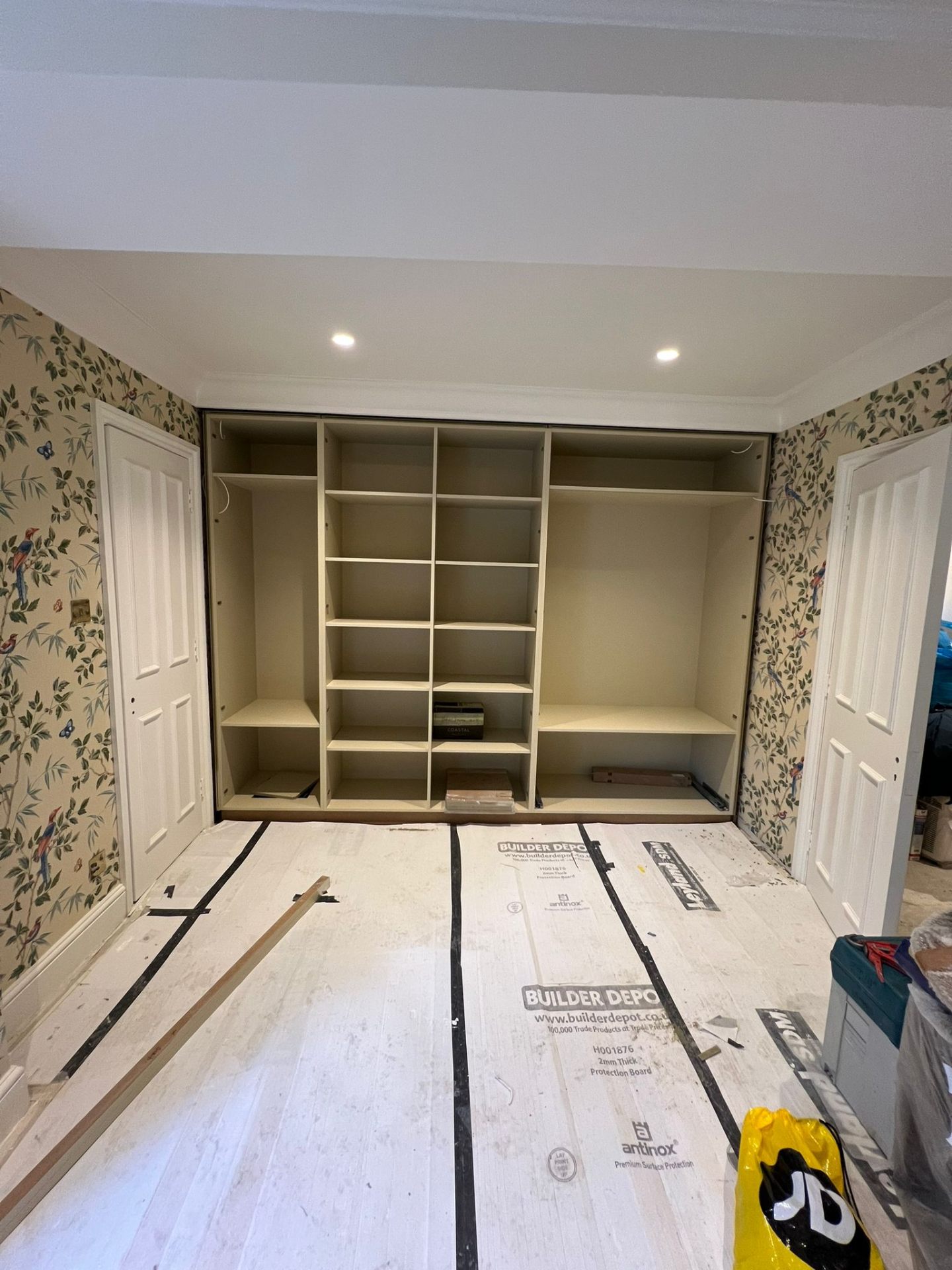 Fitted wardrobe frame being installed against bird-patterned wallpaper, showing the internal shelving layout — Ash Villa on-site