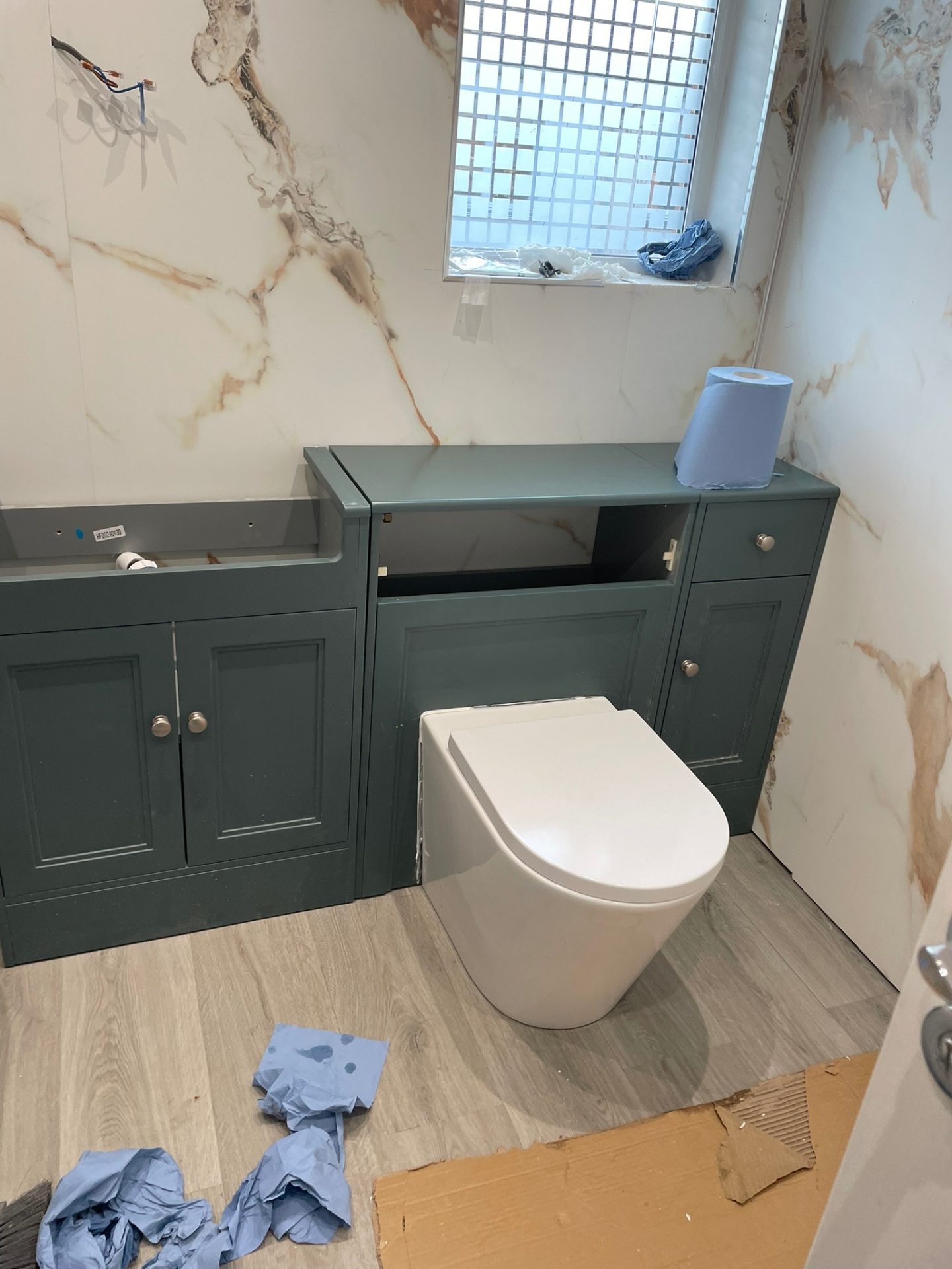 Bathroom fit-out in progress with sage green fitted vanity and WC units against large marble-veined wall tiles