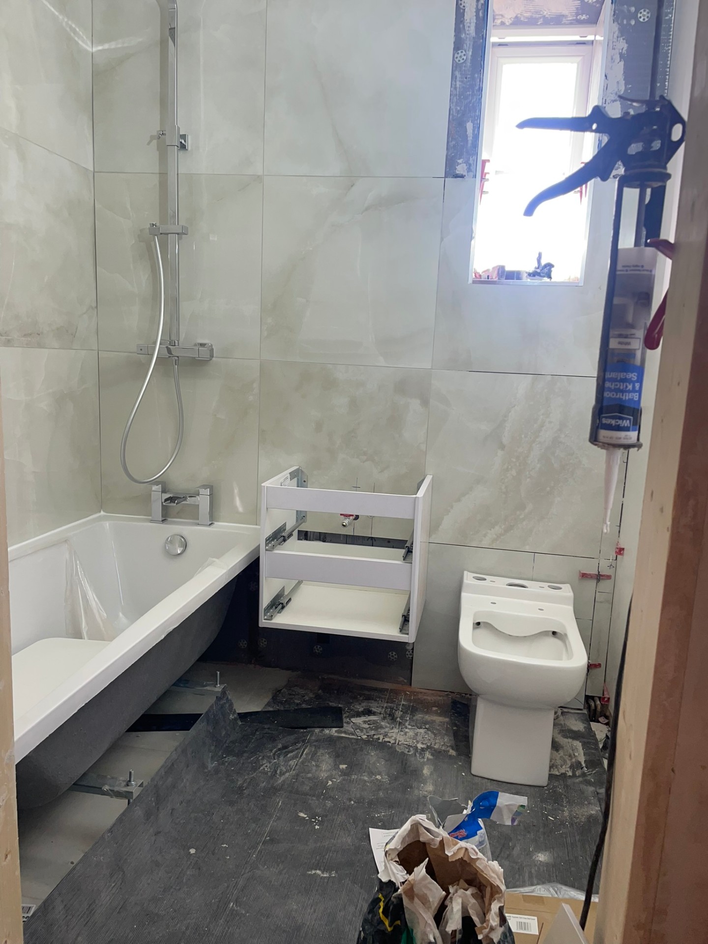 Bathroom installation in progress showing new bath, tiled marble-effect walls and WC ready for vanity fitting