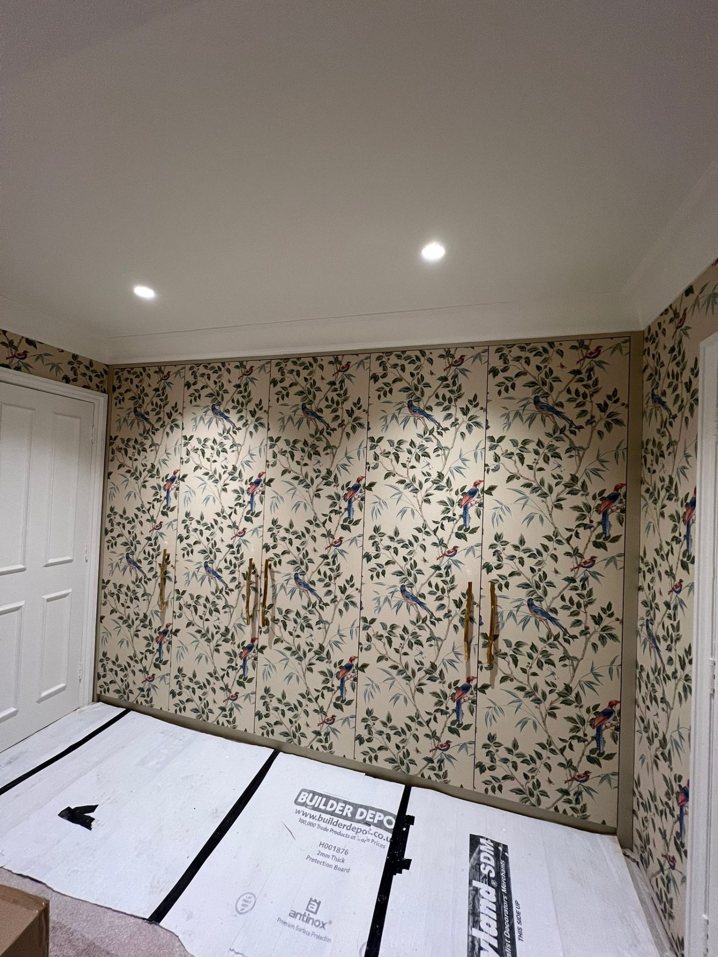 Bespoke fitted wardrobe with bird-and-branch patterned wallpaper door panels and internal spotlights — Ash Villa refurbishment joinery, West London